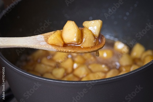Bamboo spoon with cooked apple pieces above casserole pot with apple compote