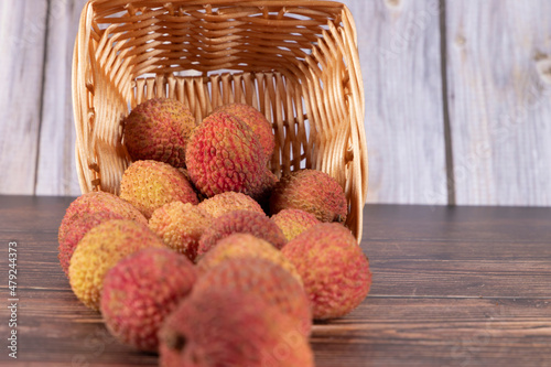 Overturned basket with tasty Lychee (Litchi chinensis, scientific name in Latin), with blurred foreground, on wood. Selective focus.
