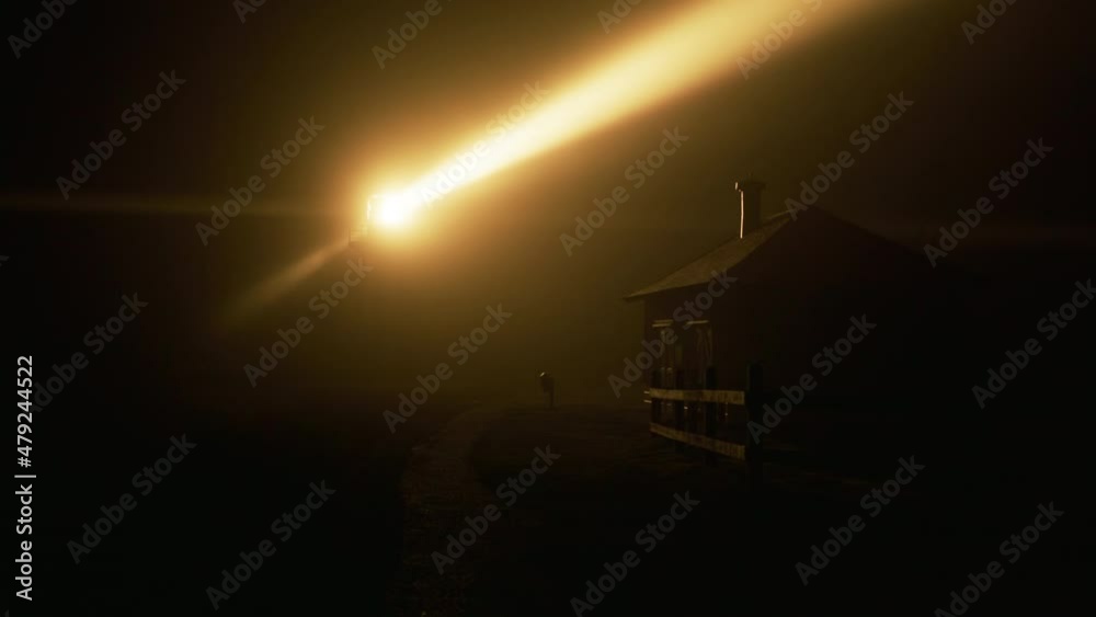 Rotating beam of Light house lantern illuminating thick fog cloud swirling around by yellow light, shot on RED camera. Night scene on marine light house, historic building landmark nature coastal park