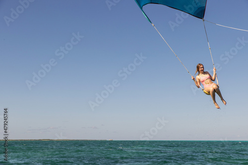 Girl flying over the Caribbean sea during fun activity with a spinnaker parachute ride. The wind is lifting her into the air as she holds on to the kite. photo