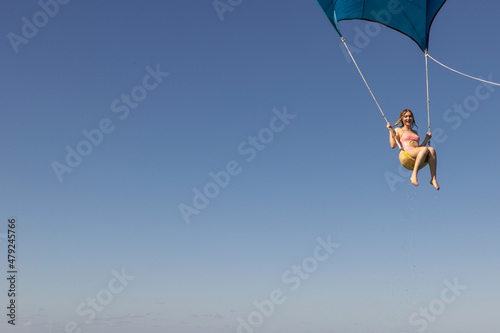 Girl flying over the Caribbean sea during fun activity with a spinnaker parachute ride. The wind is lifting her into the air as she holds on to the kite. photo