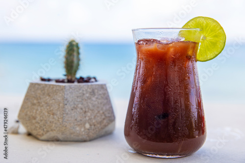 Bloody Mary cocktail garnished with fresh lime and next to a cactus plant on the beach photo