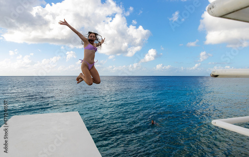Young woman jumping off diving platform into blue Caribbean sea near coast of tropical island Cozumel, Mexico during vacation.