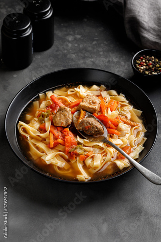 Lagman. The national Uzbek soup with noodles and pieces of meat, fried vegetables. Close up soup. Black plate and black background