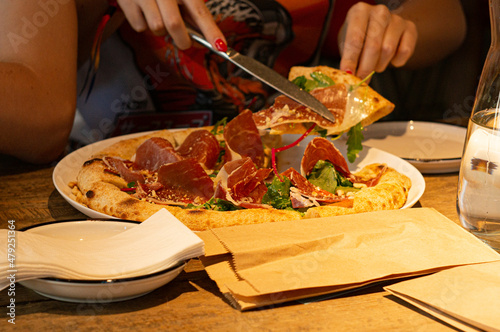 Woman taking pizza slice from the plate at the restaurant, fresh baked pizza with prosciutto and parmigiano cheese