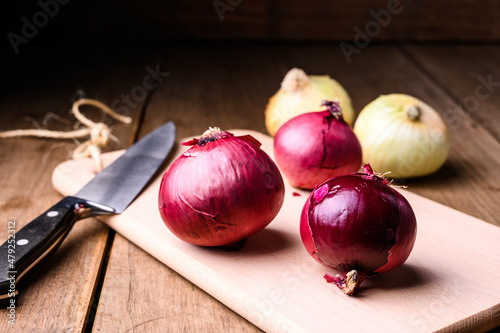 Red and white onions on a wooden chopping board and knife on a rustic wooden table in the kitchen, top view. High quality photo