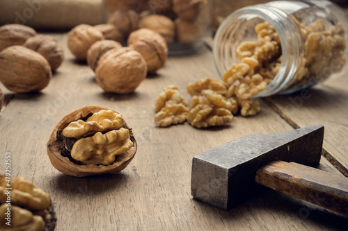 Nuts coming out of a glass jar and hammer on a wooden table in a dark environment.. High quality photo