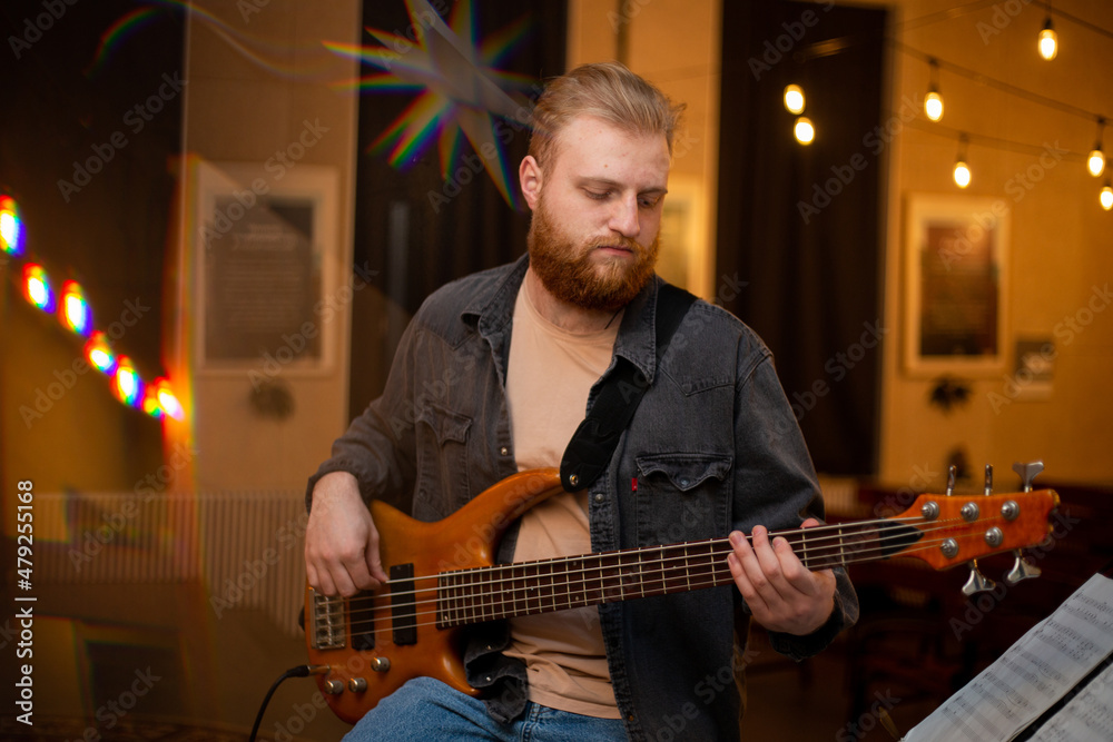 Obraz premium A young guy with a beard plays a bass guitar with five strings