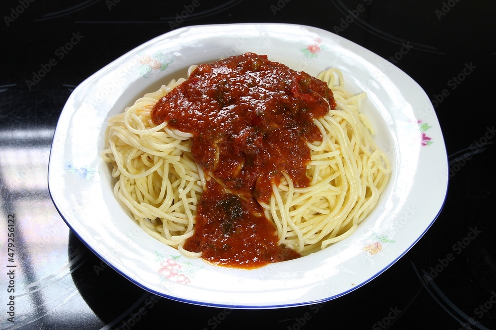 On a black ceramic cooktop, a spaghetti bolognese dish is isolated on a white plate. Shallow depth of field, selective focus