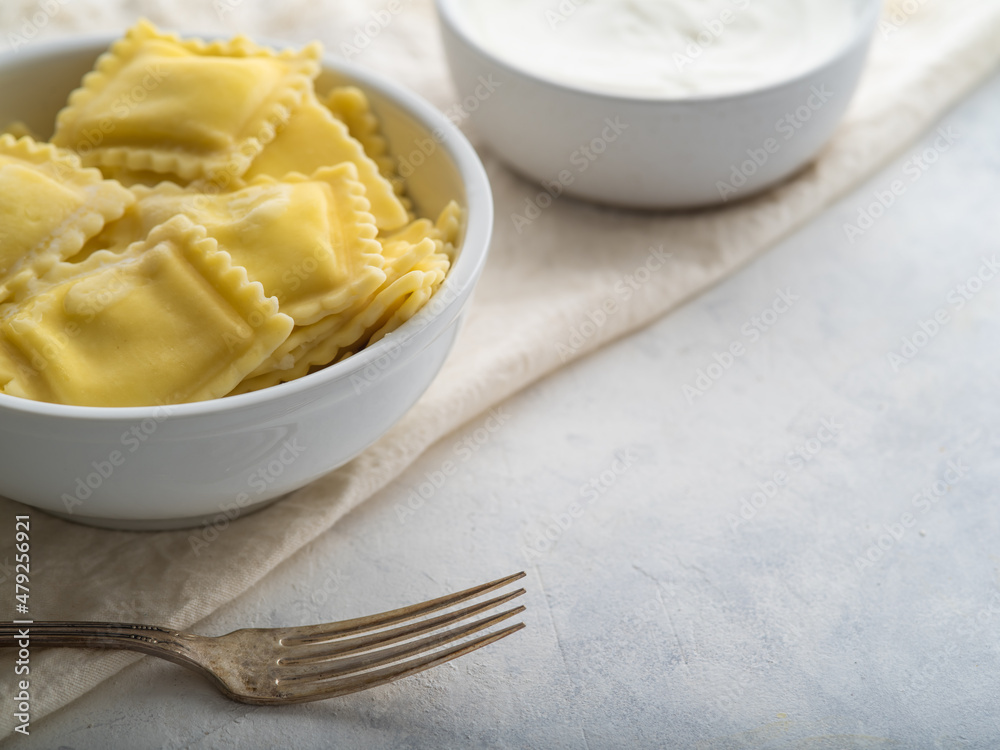 Serving of Italian ravioli, fork and sour cream sauce on a white plate. Pastel shades. There are no people in the photo. Close-up. Restaurant, hotel, cafe, home cooking, culinary blog. Serving of Italian ravioli, fork and sour cream sauce on a white plate. Pastel shades. There are no people in the photo. Close-up. Restaurant, hotel, cafe, home cooking, culinary blog.