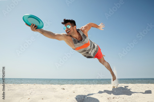 Photos Sportive man jumping and catching flying disk at beach