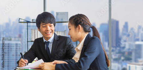 Asian business people wearing formal suit are discussing over the annual report in formal business office with modern cityscape on the background with copy space