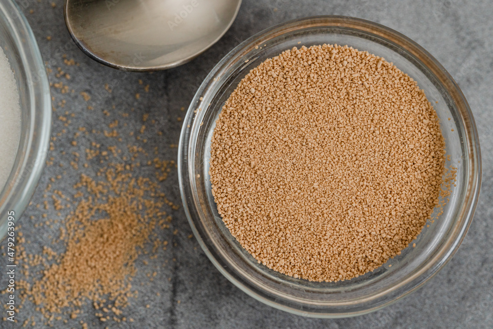 Dry yeast and sugar in a glass bowls close up on grey marble background, copy space, flat lay. Dry yeast and sugar in a glass bowls close up on grey marble background, copy space, flat lay.