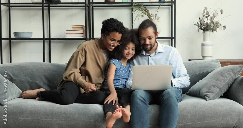Young African couple and little daughter looking at laptop screen talking, choose goods and services on internet, discuss on-line purchase sit on sofa at home. Family leisure use modern tech concept Young African couple and little daughter looking at laptop screen talking, choose goods and services on internet, discuss on-line purchase sit on sofa at home. Family leisure use modern tech concept