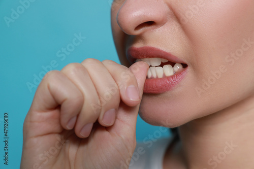 Young woman biting her nails on light blue background, closeup