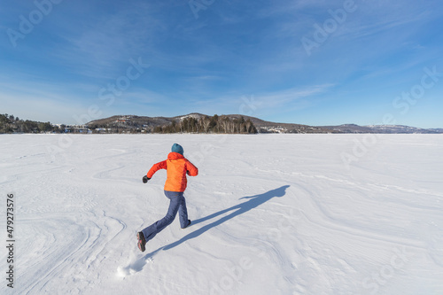 Winter fun in snow. Woman running on frozen lake in snowy winter nature landscape