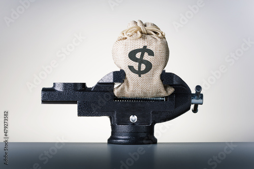 Crisis. Concept of reducing costs. Bag with dollars money in vise.