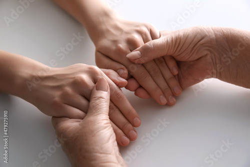 Young and elderly women holding hands together at white table, closeup