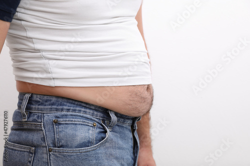 Man wearing tight t-shirt and jeans on white background, closeup. Overweight problem © New Africa