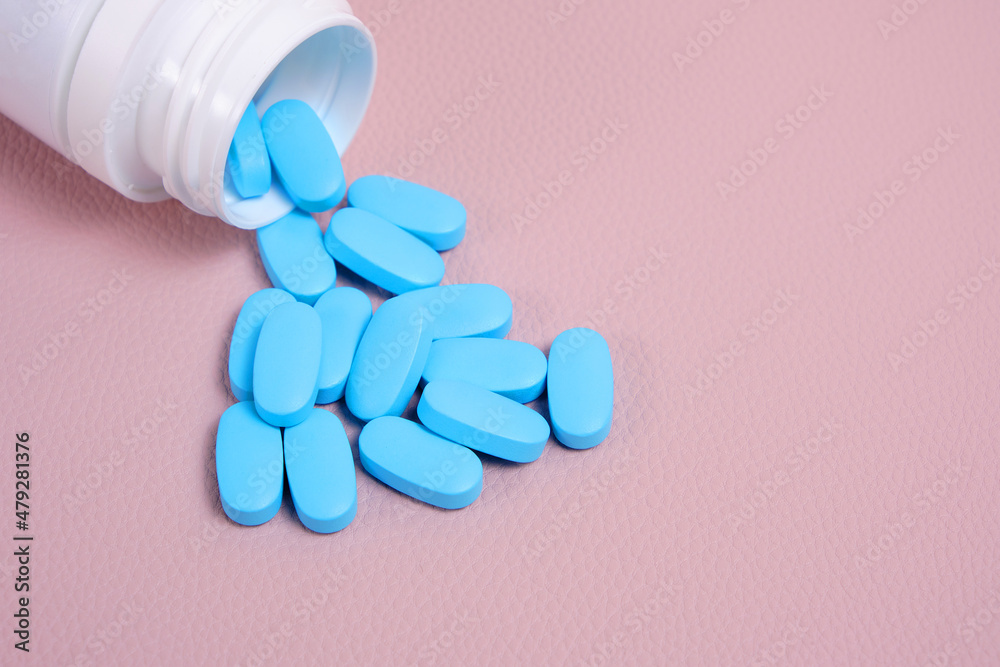 Scattering blue pills from bottle on pink background top view. Scattering blue pills from bottle on pink background top view.