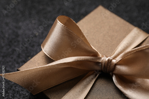 Shiny gift box with golden bow on black background, closeup