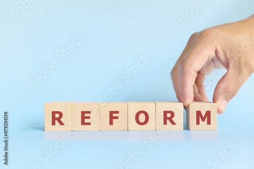 Reform concept. Hand stacking wooden blocks in blue background.
