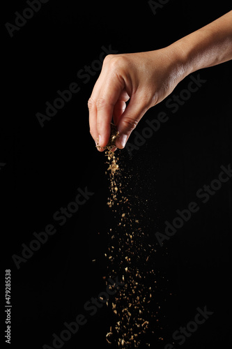 Hand sprinkling oregano on black background