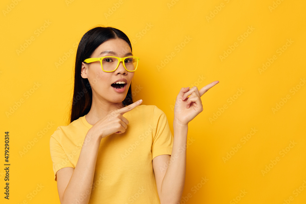 Obraz premium woman with Asian appearance in glasses gesturing with hands copy-space yellow background unaltered