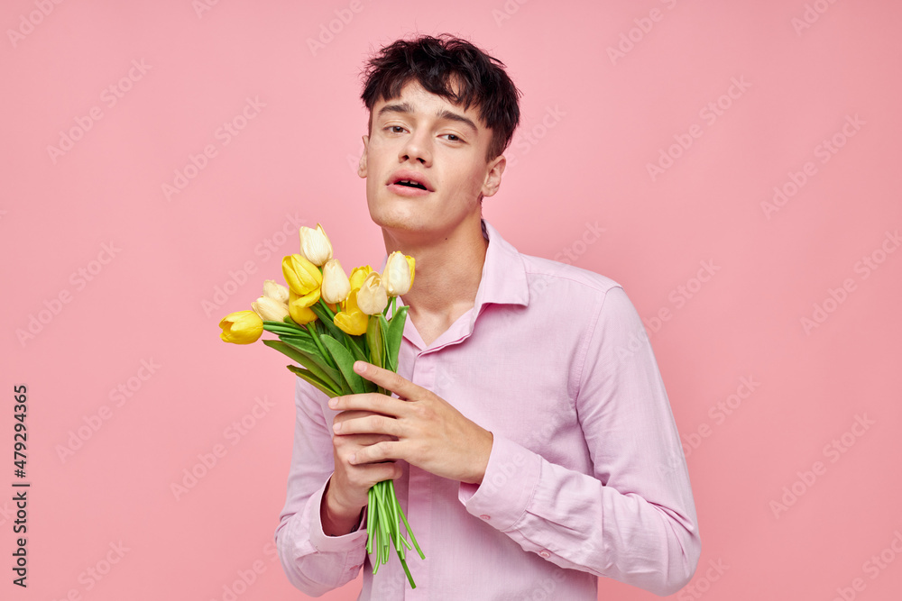 A young man in a pink shirt with a bouquet of flowers gesturing with his hands isolated background unaltered A young man in a pink shirt with a bouquet of flowers gesturing with his hands isolated background unaltered