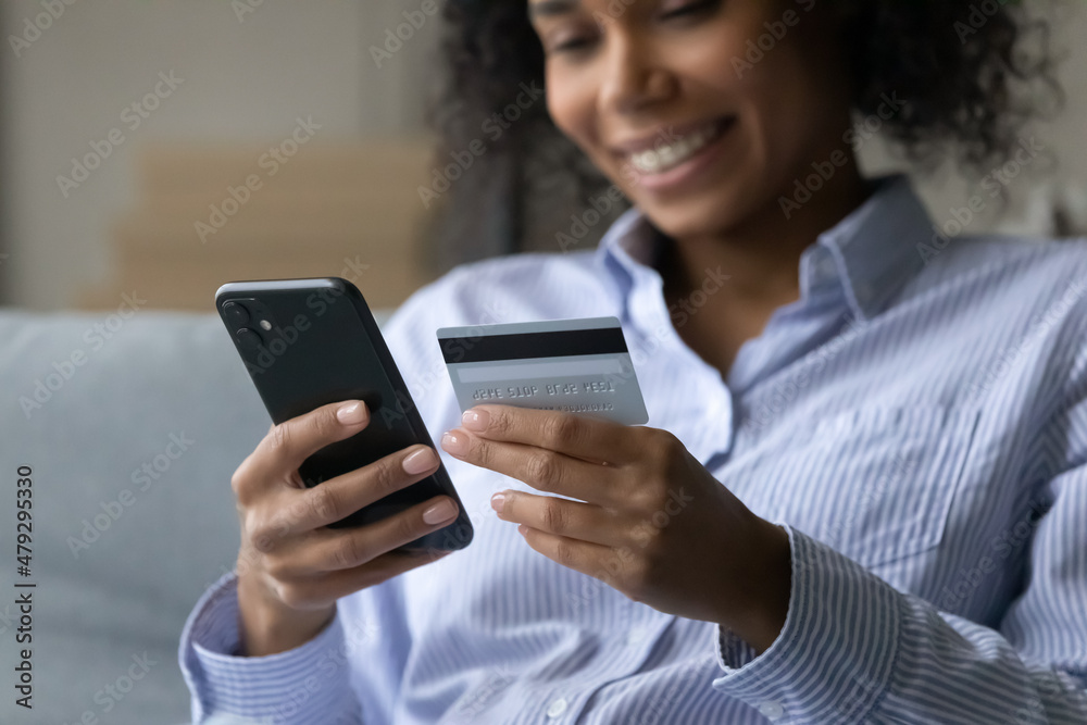 Close up smiling african ethnicity woman holding credit card in hands, involved in shopping in internet store, purchasing goods or services online, satisfied with fast money transfer secure payments. Close up smiling african ethnicity woman holding credit card in hands, involved in shopping in internet store, purchasing goods or services online, satisfied with fast money transfer secure payments.