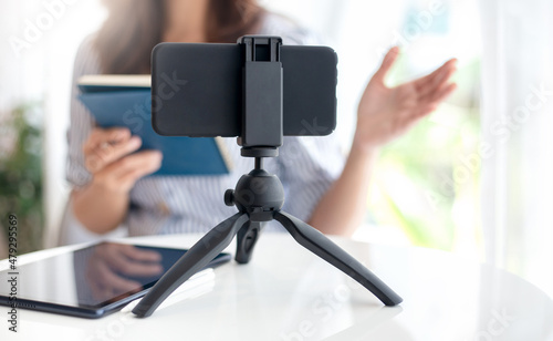 Focus on modern smartphone gadget on tripod, young asian woman in casual colthes making live broadcast on Internet to coaching and working online at home, Concept working at home with new normal