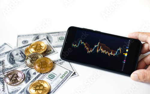 Focus on bitcoin with bank note and blurred trading chart on mobile screen in hand. Concept trading on the cryptocurrency exchange and white background