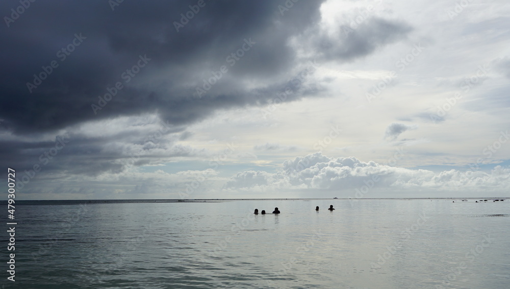 Swimming people under stormy sky with dark clouds before rain at a quiet beach in Saipan 