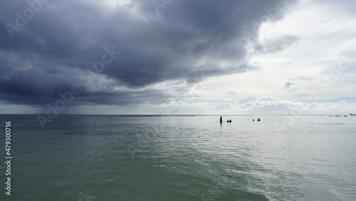 Swimming people under stormy sky with dark clouds before rain at a quiet beach in Saipan 