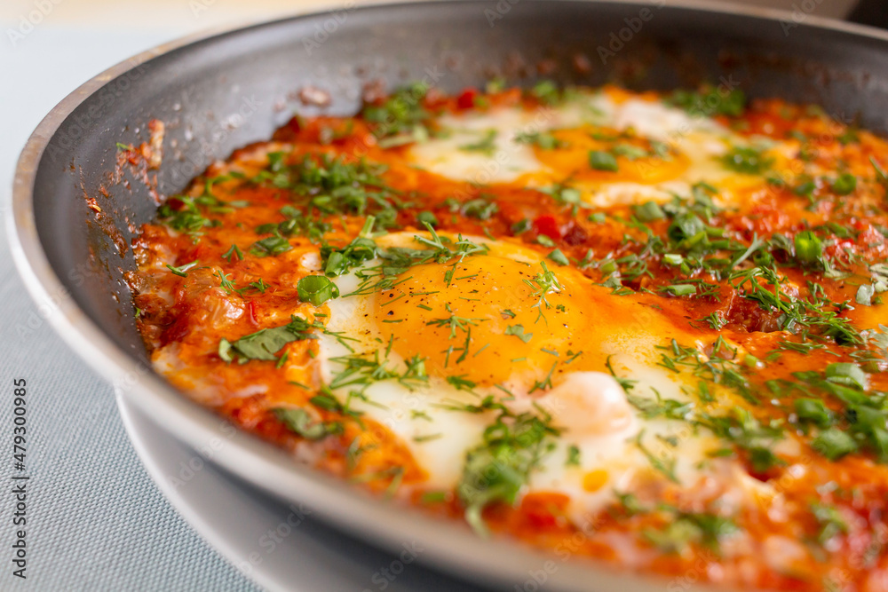 Shakshuka in a pan. Middle eastern traditional breakfast dish. Fried eggs with tomatoes, pepper, vegetables and herbs. Close up.