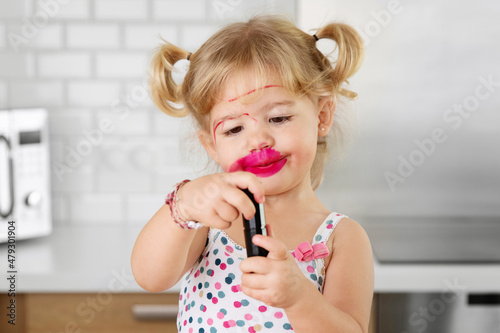 Smiling toddler girl with messy face holding lipstick