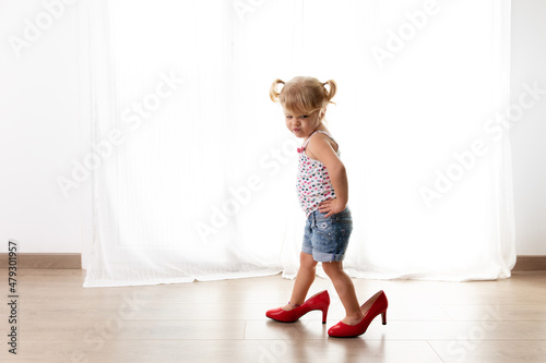 Toddler girl with funny attitude walking with mother's high heels photo