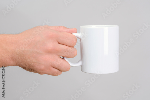 white mug in a man's outstretched hand on a gray background