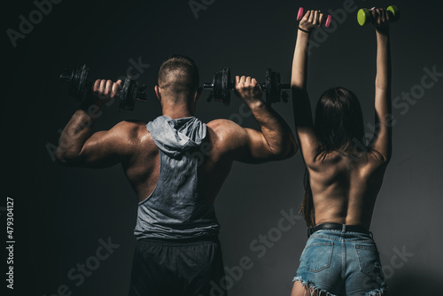 Sexy sport couple exercising with dumbbell. Muscular man with naked body, fitness woman with dumbbells on a dark background, back view. Slim sexy girl with strong muscular man workout.