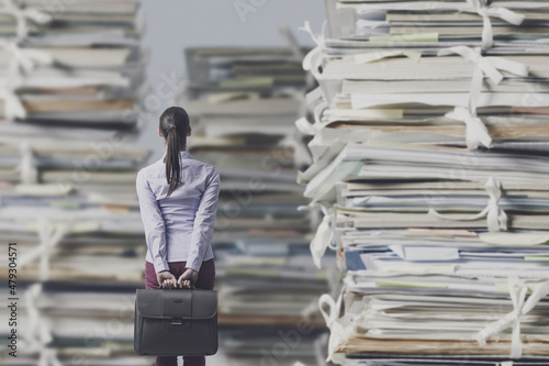 Frustrated businesswoman looking at piles of paperwork photo