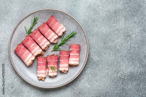 Raw smoked bacon in a plate with rosemary on gray concrete grunge background. Top view, flat lay, copy space.