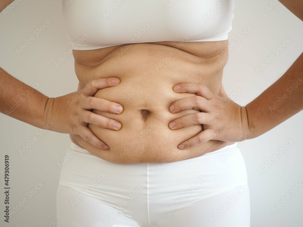 Woman holding fold of skin, cellulite on female body, on white background. closeup photo, blurred.
