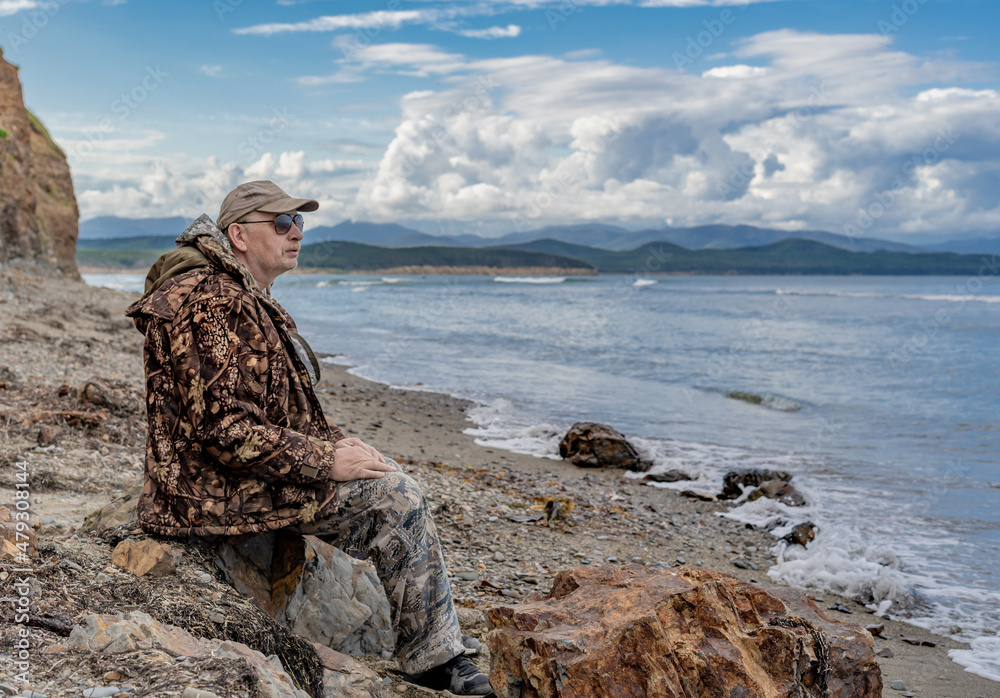 Portrait of a pensive elderly man on the seashore looking at the sea against the backdrop of rocks thinking about the meaning of life.imagination and vision of a happy future. Portrait of a pensive elderly man on the seashore looking at the sea against the backdrop of rocks thinking about the meaning of life.imagination and vision of a happy future.