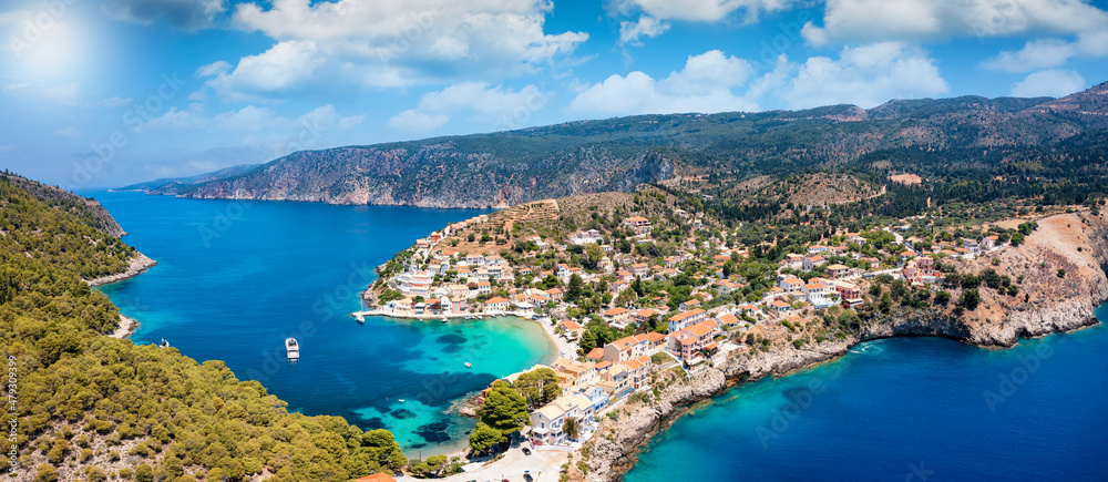 Panoramic aerial view of the little village of Assos on the island of Kefalonia, Greece, with emerald, calm sea and cloudy sky