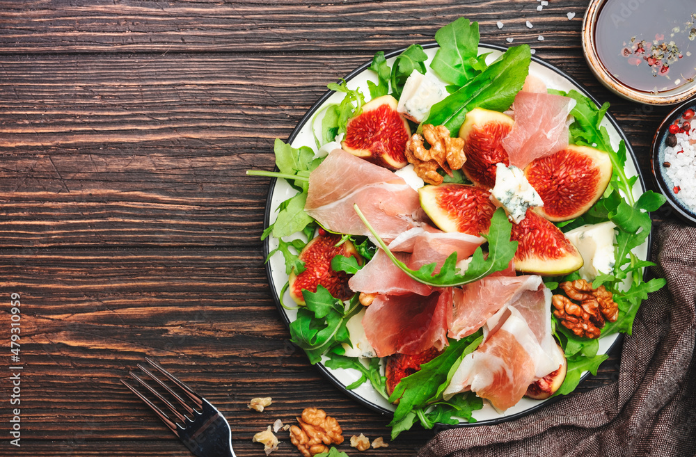 Summer fig salad with jamon, blue cheese, walnuts, arugula on old wooden kitchen table background, top view, copy space