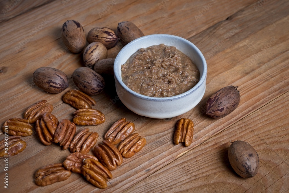 Organic pecan nut butter in bowl with raw pecans on a wooden table Organic pecan nut butter in bowl with raw pecans on a wooden table