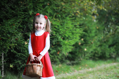 A little girl in a red hat and dresses is walking in the park. Cosplay for the fairytale hero  Little Red Riding Hood 