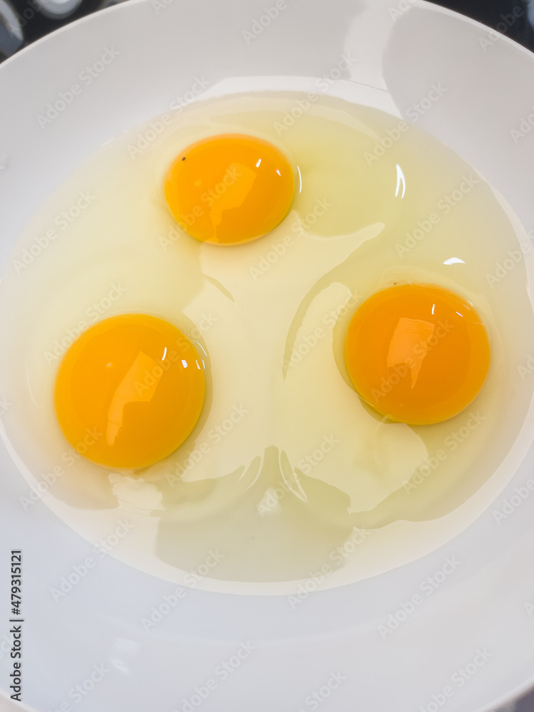 Three bright yellow raw chicken eggs in a white bowl. Three bright yellow raw chicken eggs in a white bowl.