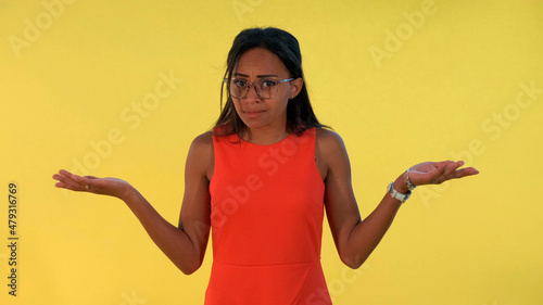 Mixed-race young woman spreading her hands to the sides and saying what on yellow background. She opened her eyes widely.