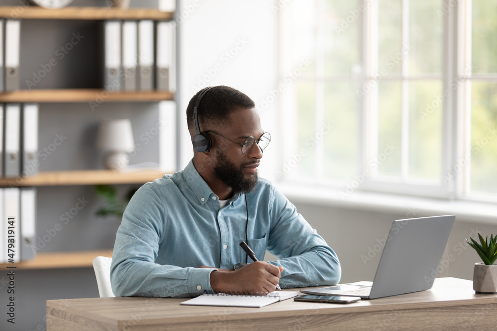 Calm millennial african american male with beard in glasses and headphones watches video lesson on pc